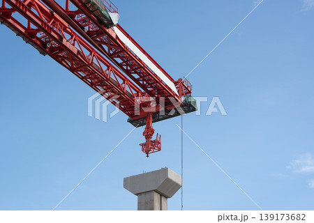 Close up red tower crane lifting concrete pillar against blue sky construction site heavy industry engineering structure and urban development concept Close up red tower crane lifting concrete pillar against blue sky construction site heavy industry engineering structure and urban development concept 139173682