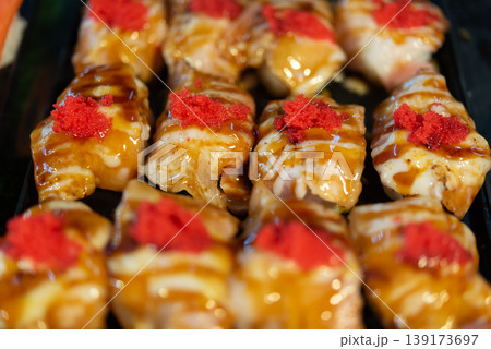 Close up pork sushi rolls topped with spicy roe and sauce on black tray rich flavor glossy texture appetizing Japanese style cuisine and natural light 139173697