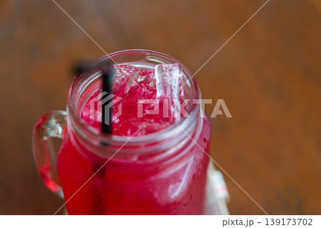 Close up red iced drink in glass jar with ice cubes and straw refreshing cold beverage sweet fruity flavor on wooden table summer refreshment concept Close up red iced drink in glass jar with ice cubes and straw refreshing cold beverage sweet fruity flavor on wooden table summer refreshment concept 139173702