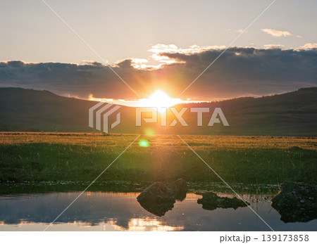 Sunrise over hills and reflection in water during early morning hours in a natural setting Sunrise over hills and reflection in water during early morning hours in a natural setting 139173858