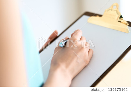 クリップボードに記入する女性の手元 139175162