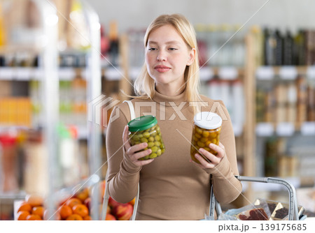 Girl buyer examine good, doubt and choose pickled olives in store 139175685