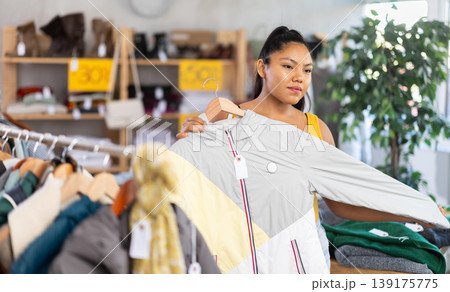Woman chooses coat for the winter period in fashionable clothing store 139175775