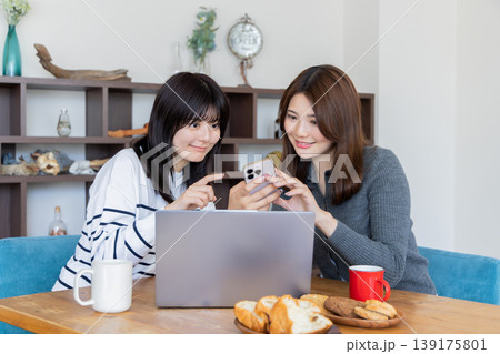 スマートフォンを一緒に楽しむ若い女性2人とノートパソコンのあるリラックスした室内シーン スマートフォンを一緒に楽しむ若い女性2人とノートパソコンのあるリラックスした室内シーン 139175801