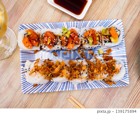On table there is plate with set of sushi - uramaki rolls with cucumber, avocado crab and salmon On table there is plate with set of sushi - uramaki rolls with cucumber, avocado crab and salmon 139175894