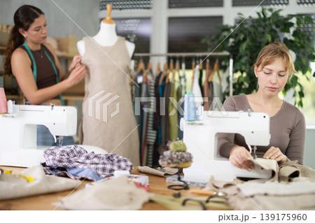 Young tailoress using sewing-machine while other working with mannequin 139175960