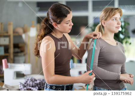 Female dressmaker taking measurements from client in sewing studi 139175962