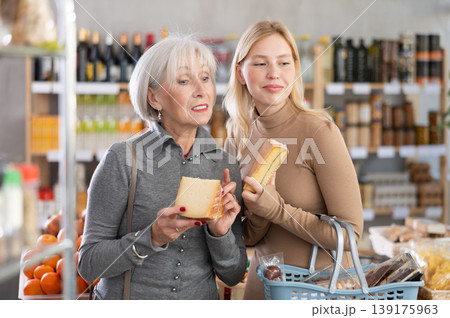 Girl and grandmother buyers examine good, doubt and choose cheese in store 139175963