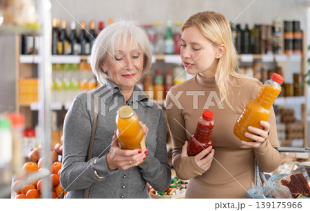 Girl and grandmother buyers examine good, doubt and choose between varieties of fruit juice in store Girl and grandmother buyers examine good, doubt and choose between varieties of fruit juice in store 139175966
