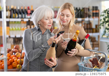 Elderly mother and her adult daughter scan a QR code on a bottle of wine label together to check expiration date Elderly mother and her adult daughter scan a QR code on a bottle of wine label together to check expiration date 139175975
