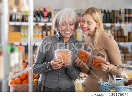 Girl and grandmother buyers examine good, doubt and choose prawn in store 139176075