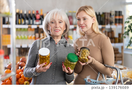 Girl and grandmother buyers examine good, doubt and choose pickled olives in store 139176089