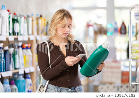 Before making purchase, girl buyer scan QR code on packaging of liquid detergent Before making purchase, girl buyer scan QR code on packaging of liquid detergent 139176182