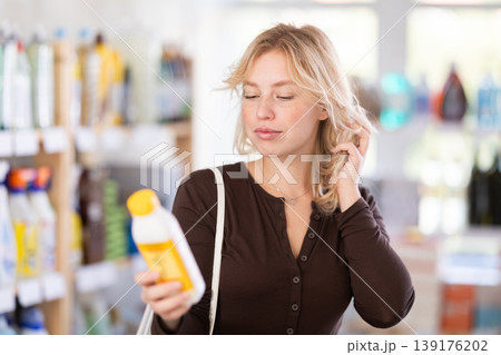 Girl housewife in household store examines goods, chooses hair care product 139176202