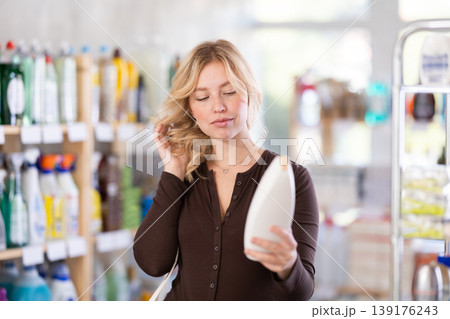 Girl housewife in household store examines goods, chooses hair care product Girl housewife in household store examines goods, chooses hair care product 139176243