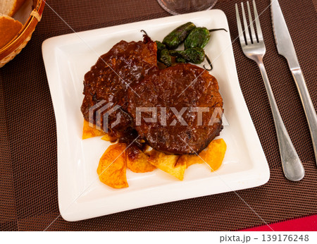 Veal roast with black sauce garnished by French fries and decorated baked green peppers. 139176248