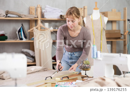 Young female dressmaker cutting textile in sewing workshop 139176255