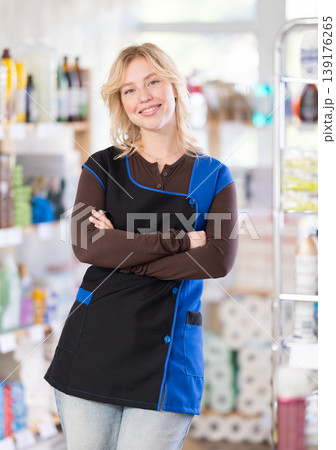 Beautiful polite young girl saleswoman standing between shelves, posing and inviting customers to hypermarket 139176265