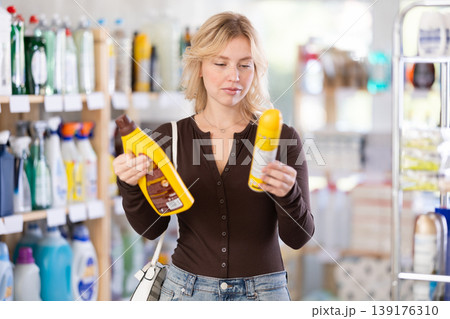 Girl housewife in household store examines goods, chooses liquid furniture polish 139176310