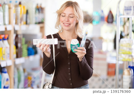 Girl housewife in household store examines goods, chooses toothpaste and related products 139176360