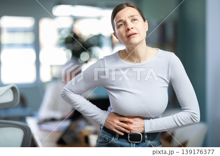 Adult woman with stomach pain during workday in office 139176377