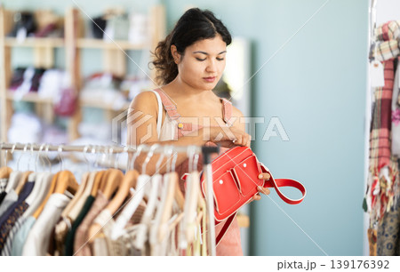 Undetermined young girl choosing handbag in clothing store Undetermined young girl choosing handbag in clothing store 139176392