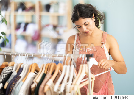 Selective young girl choosing summer dresses or tops in clothing store Selective young girl choosing summer dresses or tops in clothing store 139176403