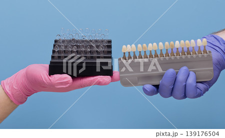 Cosmetic dentistry concept. Dentist hands holding tooth shade guide palette and transparent celluloid crown matrices for aesthetic restoration. Cosmetic dentistry concept. Dentist hands holding tooth shade guide palette and transparent celluloid crown matrices for aesthetic restoration. 139176504