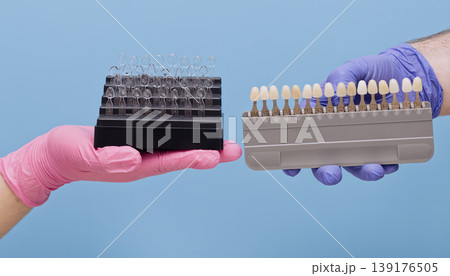 Cosmetic dental restoration tools. Hands in bright medical gloves choosing tooth color and shape over pastel blue background. Cosmetic dental restoration tools. Hands in bright medical gloves choosing tooth color and shape over pastel blue background. 139176505