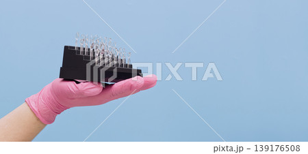 Aesthetic dentistry banner. Hand in pink glove holding transparent celluloid crown matrices for tooth restoration over blue background with wide copy space. Aesthetic dentistry banner. Hand in pink glove holding transparent celluloid crown matrices for tooth restoration over blue background with wide copy space. 139176508