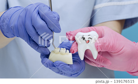 Dentists hands in blue and pink gloves holding a dental jaw model with crowns and a cute winking tooth toy character Dentists hands in blue and pink gloves holding a dental jaw model with crowns and a cute winking tooth toy character 139176515