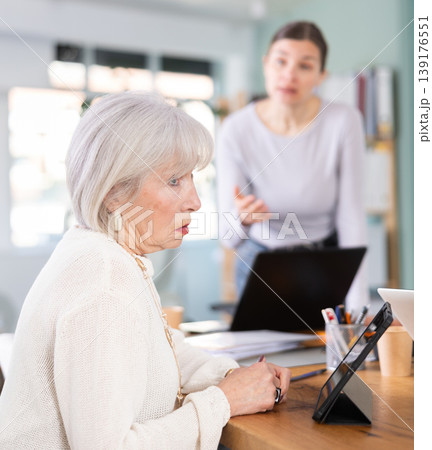 Adult woman scolding female colleague working on tablet Adult woman scolding female colleague working on tablet 139176551
