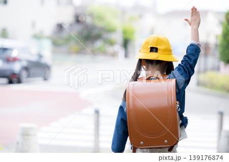 ランドセルを背負って道路の横断歩道を手をあげて渡る小学生の後ろ姿、登校や通学の交通安全イメージ顔無し ランドセルを背負って道路の横断歩道を手をあげて渡る小学生の後ろ姿、登校や通学の交通安全イメージ顔無し 139176874
