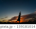 夕焼けの空を背景に音楽から元気をもらう女性のシルエット 139181014