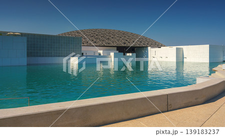 Abu Dhabi, United Arab Emirates - Jan 10 2024, Panoramic view of the snow-white facade of the Louvre Abu Dhabi with a metal dome surrounded by water, at daytime, Abu Dhabi, United Arab Emirates Abu Dhabi, United Arab Emirates - Jan 10 2024, Panoramic view of the snow-white facade of the Louvre Abu Dhabi with a metal dome surrounded by water, at daytime, Abu Dhabi, United Arab Emirates 139183237