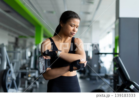 Young Black woman in gym holding her elbow with a pained expression Young Black woman in gym holding her elbow with a pained expression 139183333