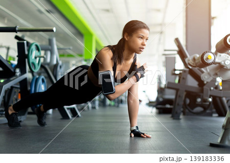 Focused young Black woman doing one arm push-up position on gym floor 139183336
