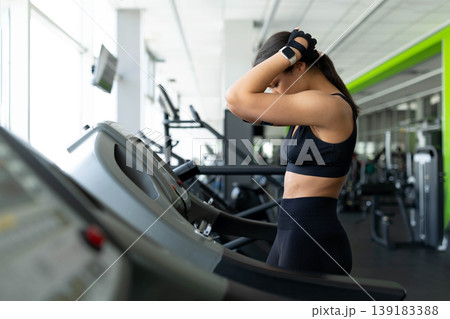 Young Black woman standing on treadmill with hands behind head looking exhausted 139183388