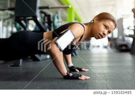 Focused Black woman doing push-ups on gym floor, wearing black sports bra Focused Black woman doing push-ups on gym floor, wearing black sports bra 139183495