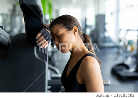 Exhausted young Black woman leaning head against gym machine with eyes closed 139183502