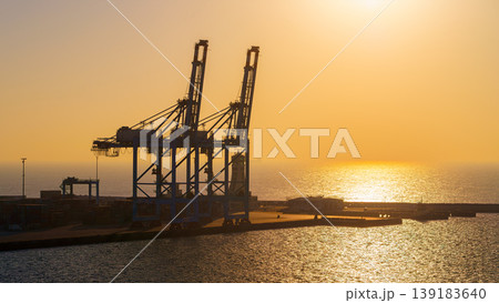 Manama, Bahrain - Jan 08 2024, Panoramic view of Bahrain commercial port with blue cranes, buildings and containers, with sea on foreground, by the morning, dawn, sunrise, Manama, Bahrain 139183640