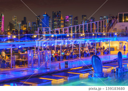 Doha, Qatar - Jan 07 2024, Panoramic view of the deck of the MSC Virtuosa cruise ship, with a part of swimming pool, skyscrapers of Doha are visible in the background, at nighttime, Doha, Qatar Doha, Qatar - Jan 07 2024, Panoramic view of the deck of the MSC Virtuosa cruise ship, with a part of swimming pool, skyscrapers of Doha are visible in the background, at nighttime, Doha, Qatar 139183680