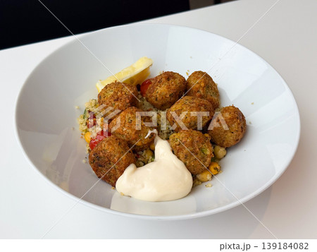Falafel balls with couscous vegetables and sauce served in a white bowl. Healthy meal, vegetarian cuisine, balanced diet, and modern food presentation 139184082