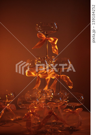 Champagne tower made of glass flutes tied with orange ribbons, illuminated by warm light, creating an elegant display for celebrations or special events Champagne tower made of glass flutes tied with orange ribbons, illuminated by warm light, creating an elegant display for celebrations or special events 139184252