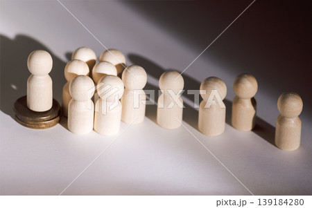 Wooden figurines representing a group of people with one figure elevated on a coin, casting shadows on a light surface, symbolizing leadership or influence Wooden figurines representing a group of people with one figure elevated on a coin, casting shadows on a light surface, symbolizing leadership or influence 139184280