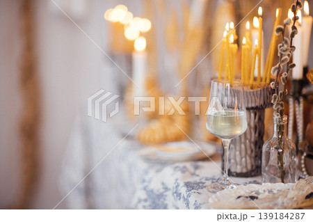 Elegant table setting with a glass of white wine, lit candles, and decorative elements for a festive celebration in a cozy indoor environment 139184287