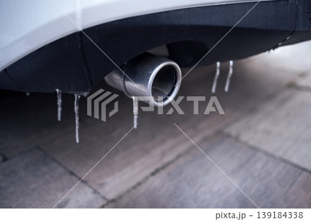 Close-up view of a car exhaust pipe with icicles hanging from it, showcasing winter conditions and the effects of cold weather on vehicles and automotive components 139184338