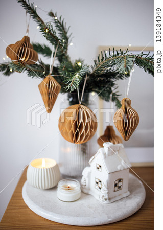 Decorative arrangement featuring honeycomb ornaments, evergreen branches, and candles on a marble tray, creating a cozy holiday atmosphere with festive charm 139184349