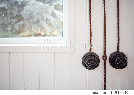 Vintage pulley system mounted on a white wooden wall beside a window, showcasing rustic charm and intricate design elements, enhancing the overall aesthetic of the interior space Vintage pulley system mounted on a white wooden wall beside a window, showcasing rustic charm and intricate design elements, enhancing the overall aesthetic of the interior space 139185309