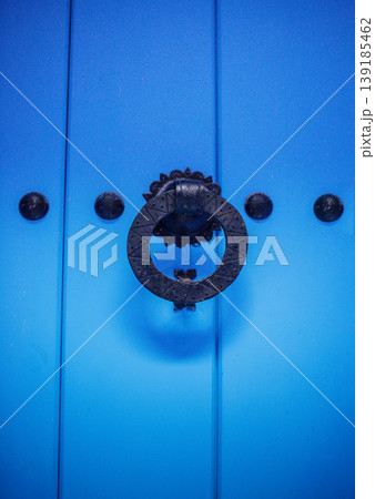 Blue wooden door with ornate black metal knocker and decorative round handle, featuring circular design elements and small round studs on the surface Blue wooden door with ornate black metal knocker and decorative round handle, featuring circular design elements and small round studs on the surface 139185462